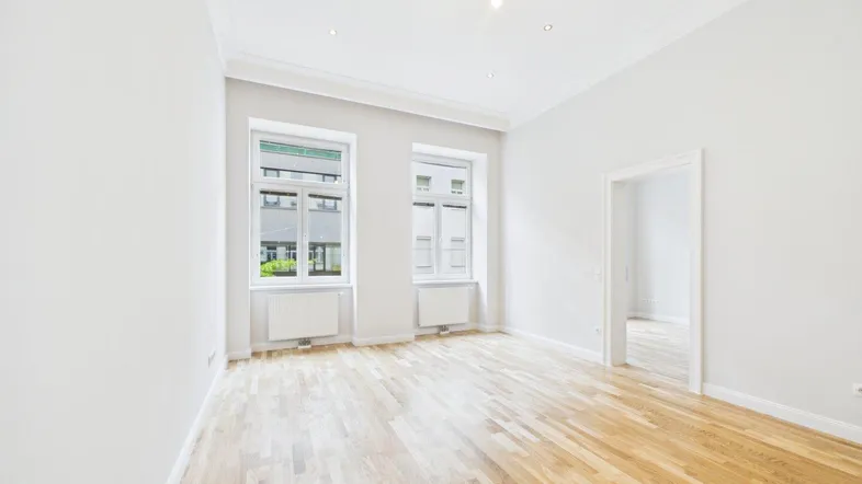 Helles Zimmer mit Parkettboden und zwei Fenstern, ideal als Wohn- oder Schlafzimmer.
