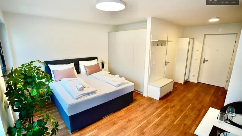 Helles Schlafzimmer in einem Studio-Apartment mit Holzboden und integriertem Kleiderschrank.