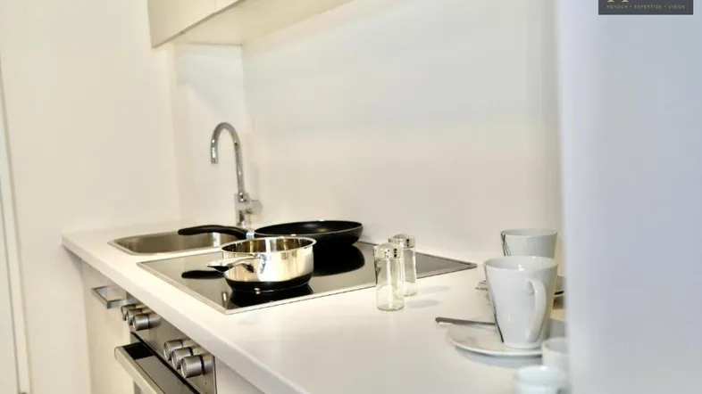 Moderne, kompakte Küchenzeile mit Induktionskochfeld und Spüle in weißem Design.