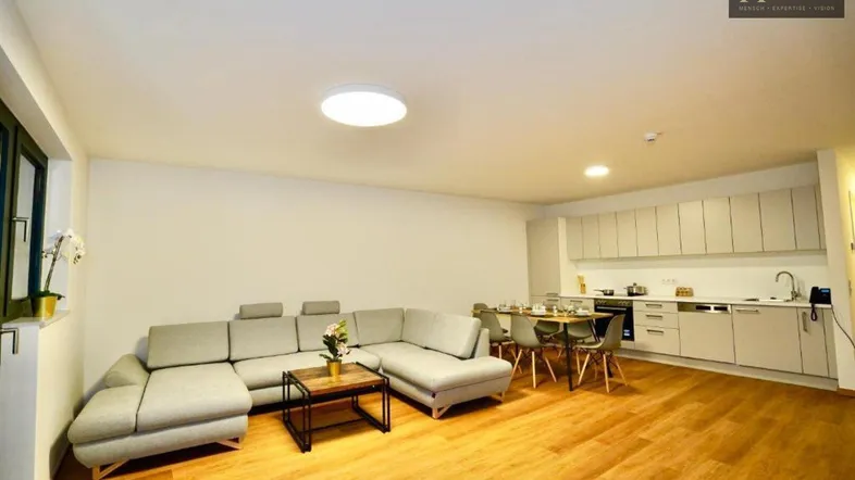 Geräumiger offener Wohn-Essbereich mit moderner Küche, bequemer Couch und Holzboden.