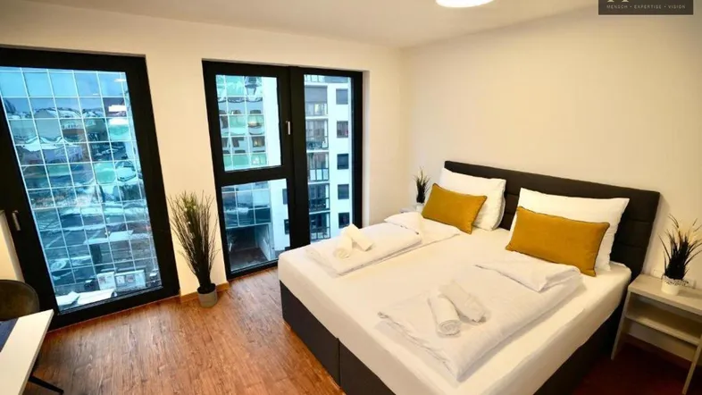 Helles Schlafzimmer mit Doppelbett, Holzboden und großen Fenstern mit Stadtblick.