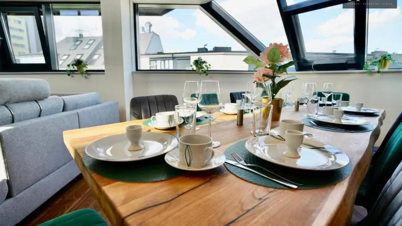 Modern gedeckter Esstisch in einem hellen Wohnbereich mit großen Fenstern und Dachblick.