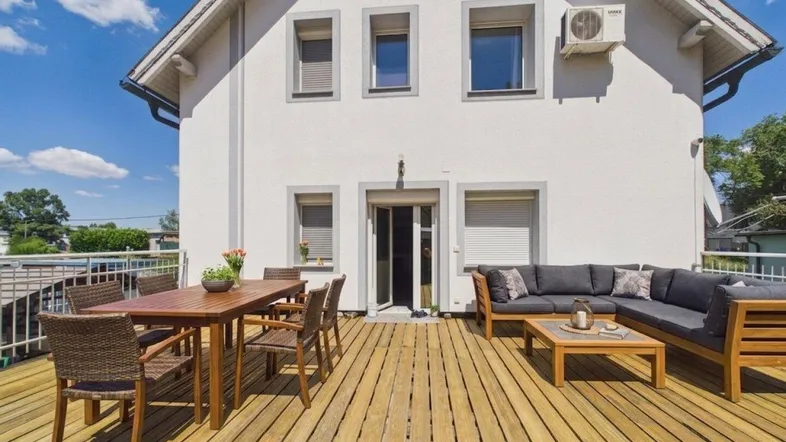 Große Holzterrasse mit Essbereich und Lounge-Möbeln vor der Hausfassade.
