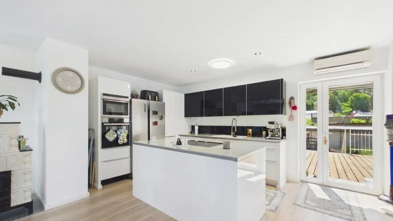 Moderne Küche mit weißer Hochglanzinsel, schwarzen Oberschränken und Zugang zur Terrasse.