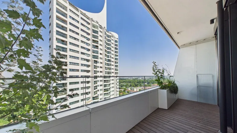 Geräumiger Balkon mit Holzboden und Glasgeländer, bietet einen weiten Blick auf die Stadt und moderne Architektur.