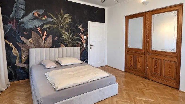 Helles Schlafzimmer mit stilvoller Tapete, Fischgrätparkett und hohen Flügeltüren.