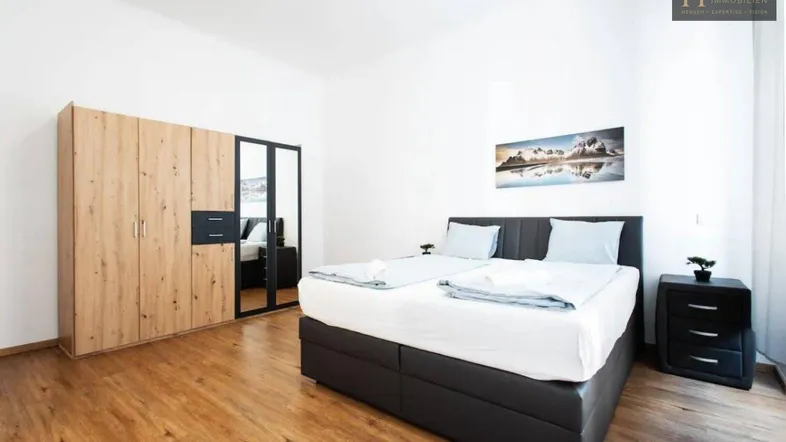 Helles Schlafzimmer mit Holzboden, großem Bett und modernem Kleiderschrank mit Spiegeltüren.