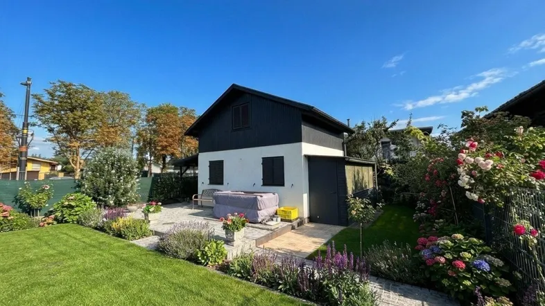 Kleines Haus mit gepflegtem Garten, blühenden Blumenbeeten und einer gemütlichen Terrasse.