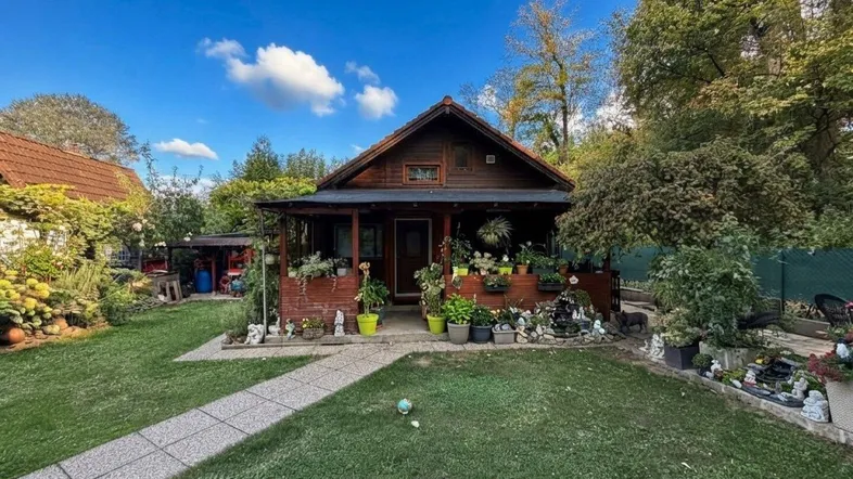 Kleines Holzhaus mit gepflegtem Garten und einem Steinweg, umgeben von viel Grün.