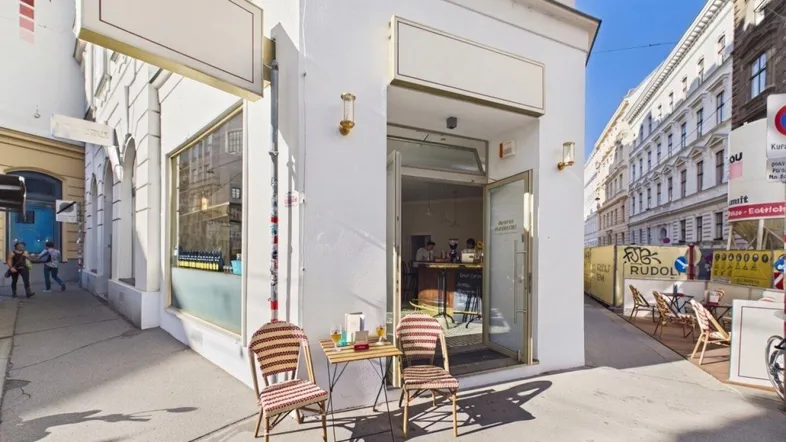 Außenansicht eines Cafés mit Tischen und Stühlen auf dem Bürgersteig, umgeben von städtischer Architektur.