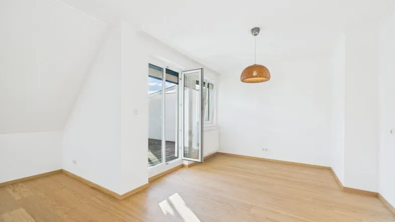 Helles Zimmer mit Holzboden, weißen Wänden und Zugang zu einem Außenbereich.