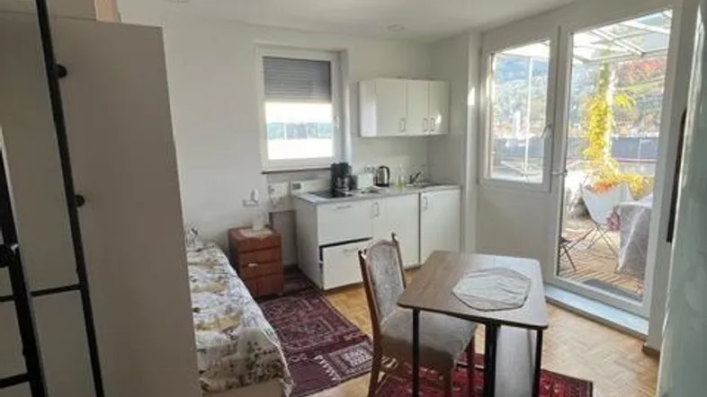 Helles Studio-Apartment mit integrierter Küchenzeile, Schlafbereich und Zugang zu einem Außenbereich.