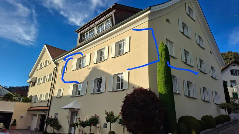 Mehrstöckiges Gebäude mit heller Fassade, vielen Fenstern und Fensterläden unter blauem Himmel.