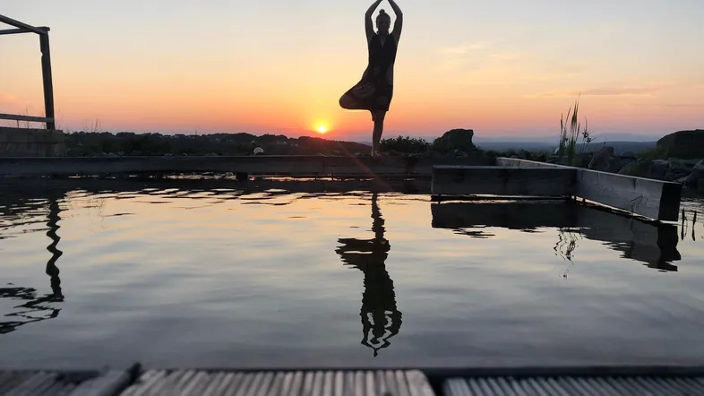Eine Person macht Yoga am Pool bei Sonnenuntergang, mit schöner Spiegelung im Wasser.