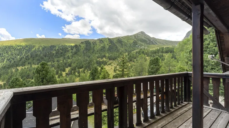 Holzbalkon mit atemberaubendem Blick auf die umliegende Berglandschaft unter blauem Himmel.
