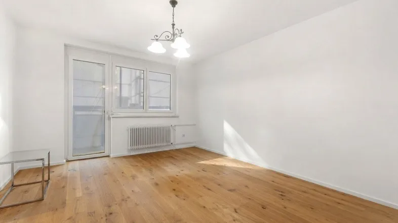 Helles Zimmer mit Holzboden, weißen Wänden und Zugang zu einem Balkon, ideal als Wohnzimmer.