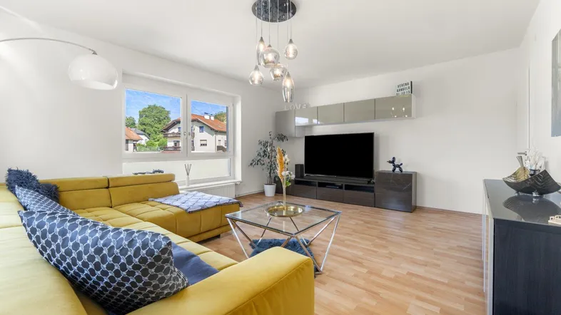 Helles Wohnzimmer mit modernem Sofa, Holzboden und Blick ins Grüne durch große Fenster.
