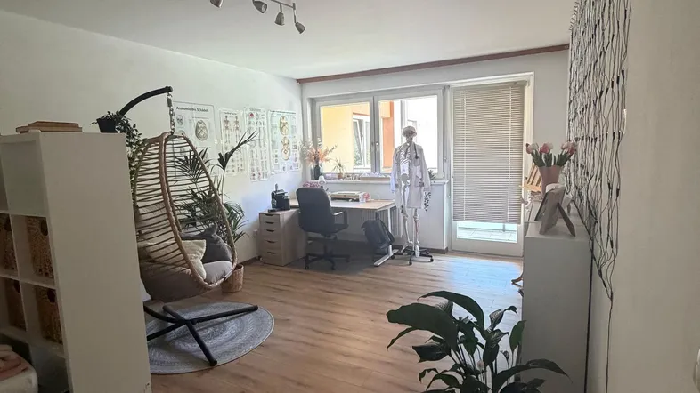 Helles Wohnzimmer mit Holzboden, Schreibtischbereich und einem gemütlichen Hängesessel am Fenster.