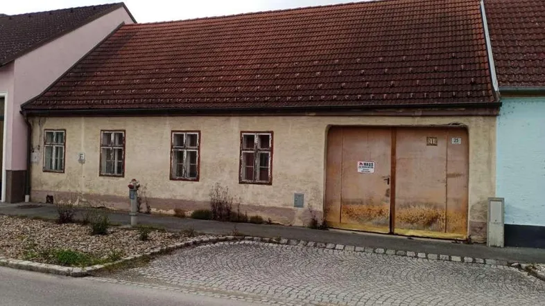 Altes Gebäude mit verputzter Fassade, kleinen Fenstern und großem Scheunentor zur Straße hin.