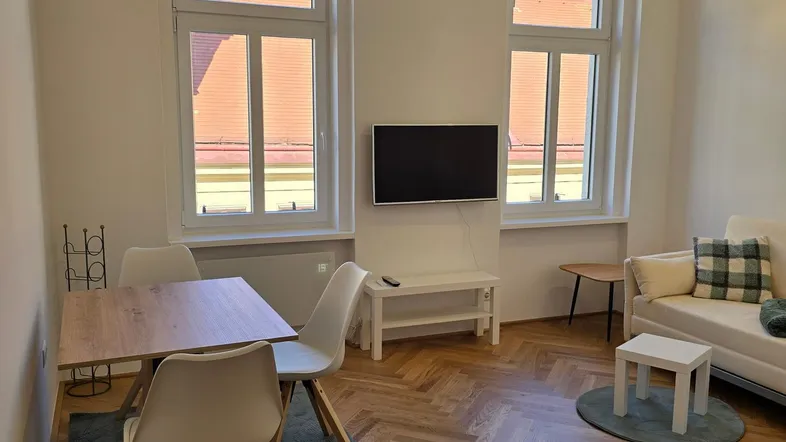 Heller Wohn- und Essbereich mit Fischgrätparkett, großen Fenstern und moderner Einrichtung.