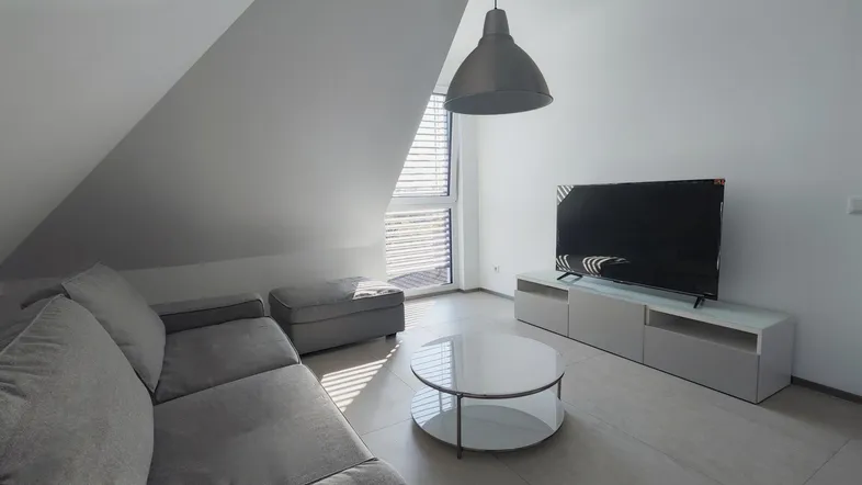 Helles Wohnzimmer mit modernem Sofa, Fernseher und schrägen Decken im Dachgeschoss.