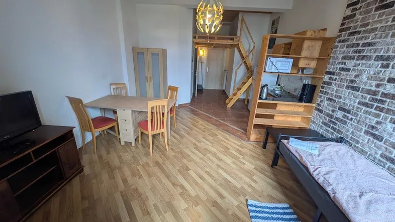 Gemütlicher Wohn- und Essbereich mit Holzboden, Esstisch und Zugang zu einem Hochbett.