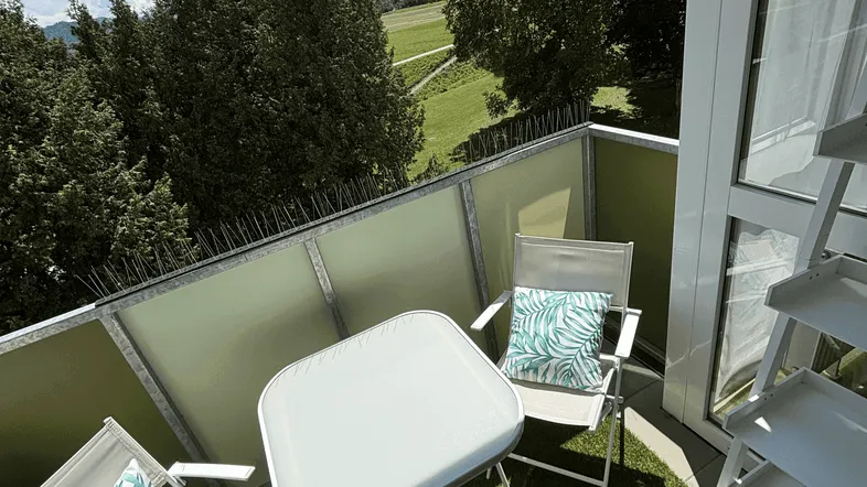 Heller Balkon mit Kunstrasen, Gartenmöbeln und weitem Blick ins Grüne.