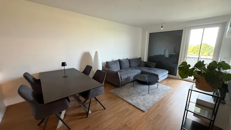 Heller Wohn-Essbereich mit modernem Sofa, Esstisch und Zugang zum Balkon, ausgestattet mit Holzfußboden.
