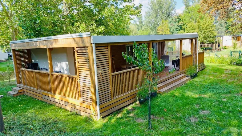 Modernes Holzchalet mit großer überdachter Terrasse, umgeben von viel Grün und Bäumen.