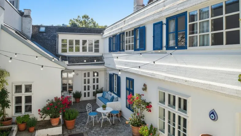 Idyllischer Innenhof mit mediterranem Flair, blauen Fensterläden und gemütlicher Sitzgelegenheit unter Lichterketten.