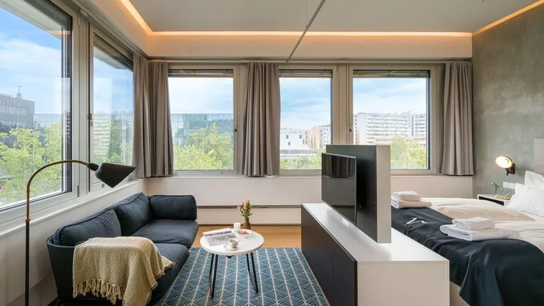 Helles Studio-Apartment mit kombiniertem Wohn- und Schlafbereich, großen Fenstern und Stadtblick.
