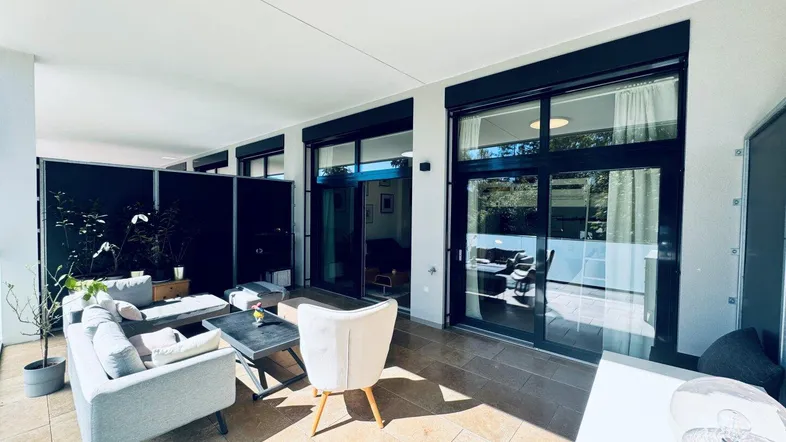 Geräumige, überdachte Terrasse mit modernen Loungemöbeln und Blick ins Grüne.