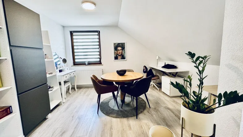 Helles Dachzimmer mit Esstisch, Arbeitsbereich und schrägen Wänden, ideal für vielseitige Nutzung.