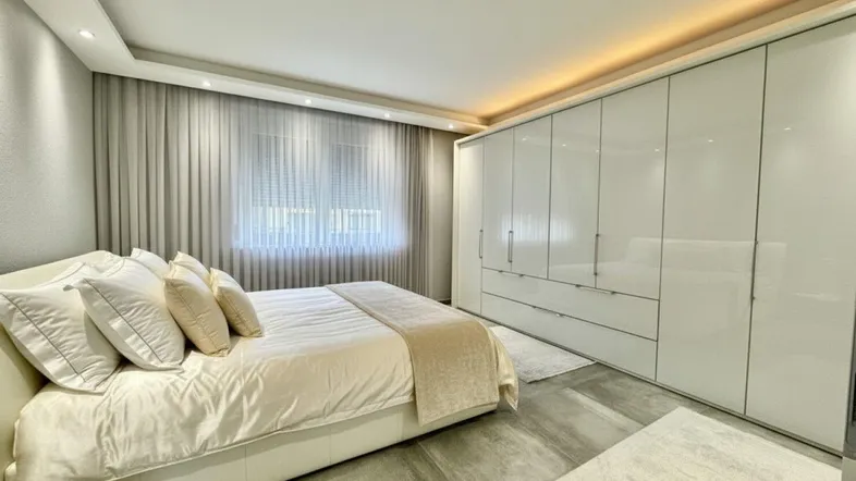 Helles Schlafzimmer mit großem Bett, Einbauschränken und indirekter Beleuchtung für eine moderne Atmosphäre.