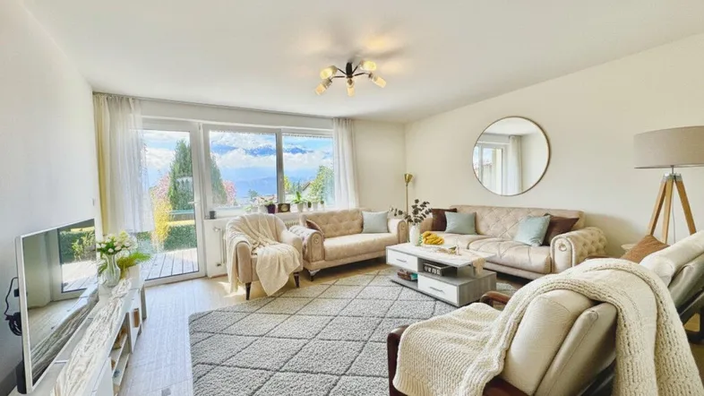 Helles Wohnzimmer mit beigen Sofas, großem Teppich und Zugang zu einem Balkon mit Aussicht.