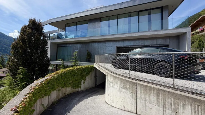 Moderne Architektur mit Zufahrt zur Tiefgarage und Bergblick in alpiner Umgebung.