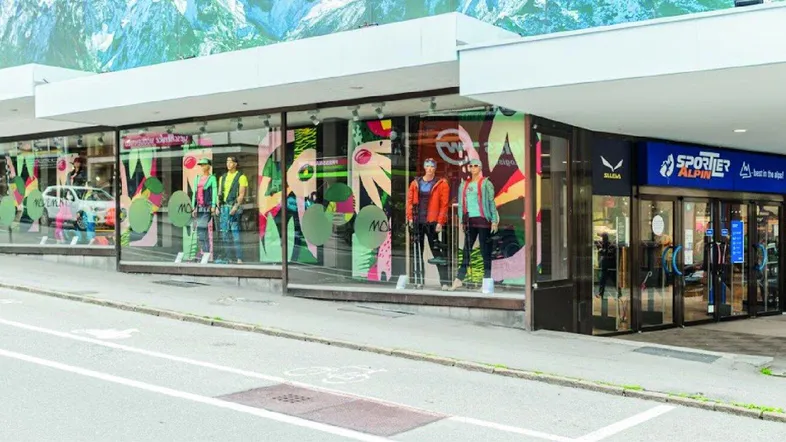 Moderne Ladenfassade mit großen Schaufenstern und einem markanten Baumstamm als Dekoration.