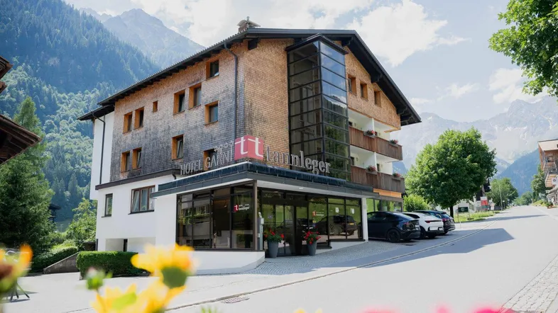 Modernes Hotelgebäude mit Holzfassade und Glasanbau, umgeben von alpiner Berglandschaft.