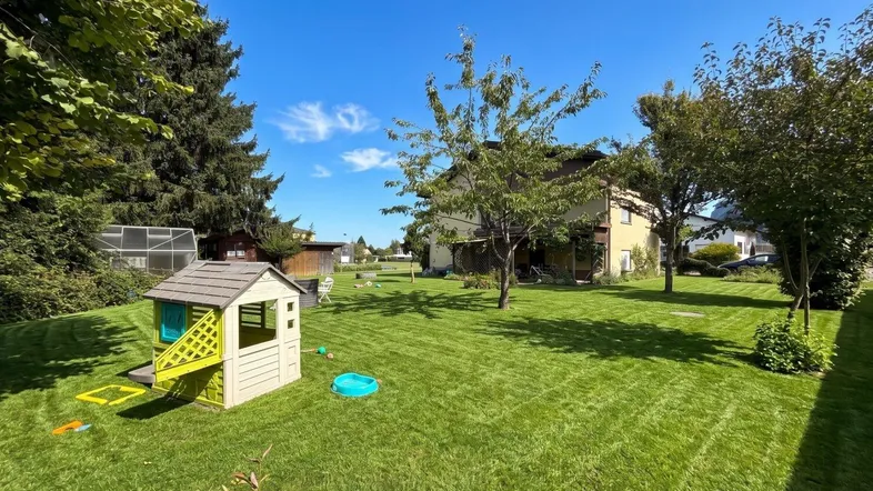 Weitläufiger, gepflegter Garten mit Kinderspielhaus und viel Rasenfläche für Freizeitaktivitäten.