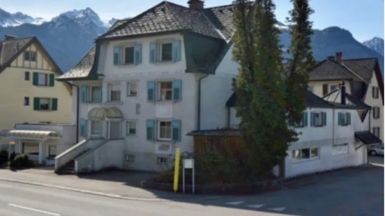Traditionelles Gebäude mit hellblauen Fensterläden und einem beeindruckenden Bergpanorama im Hintergrund.