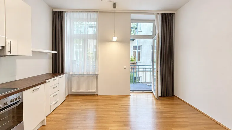 Heller Wohnbereich mit offener Küche, Holzboden und Zugang zu einem Balkon.