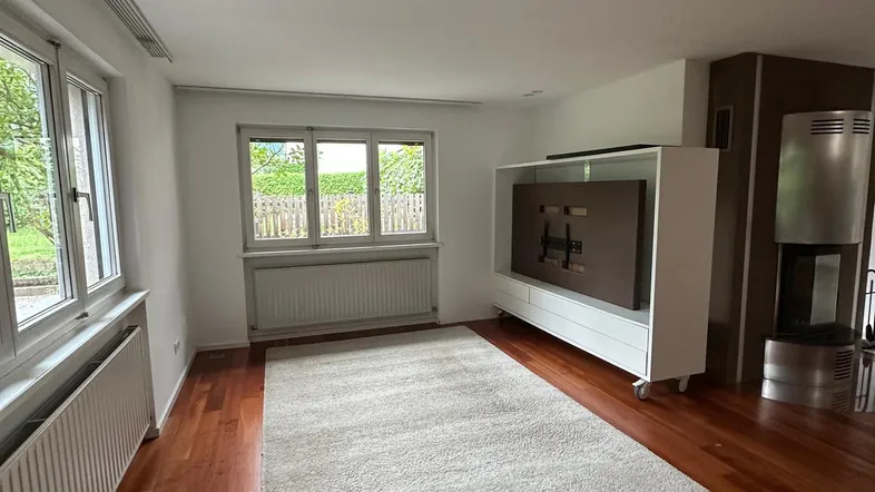 Helles Wohnzimmer mit Holzboden, großem Fenster und modernem Kaminofen.