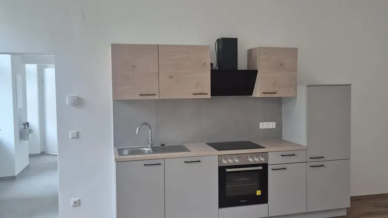 Neue Einbauküche mit hellen Holz- und grauen Fronten, ausgestattet mit Herd und Spüle.