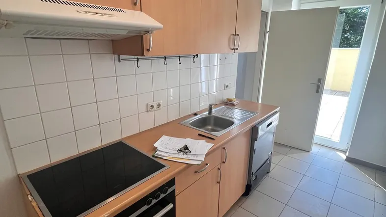 Funktionale Küche mit hellen Holzschränken, Fliesenboden und direktem Zugang zum Außenbereich.