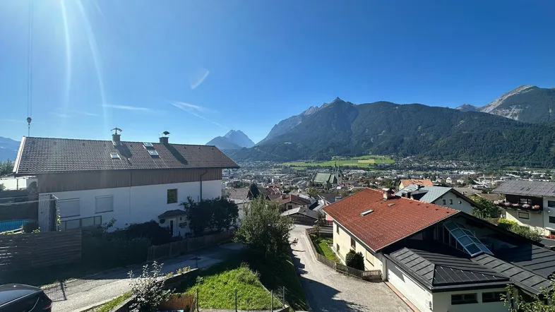 Sonniger Ausblick auf die umliegende Stadt und die majestätische Berglandschaft unter blauem Himmel.