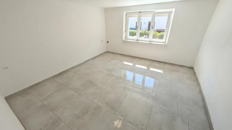 Heller, leerer Raum mit modernen grauen Fliesen und einem Fenster, das Tageslicht hereinlässt.