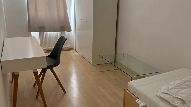 Helles Schlafzimmer mit Laminatboden, Schreibtisch und Kleiderschrank, ideal für Studenten oder Einzelpersonen.