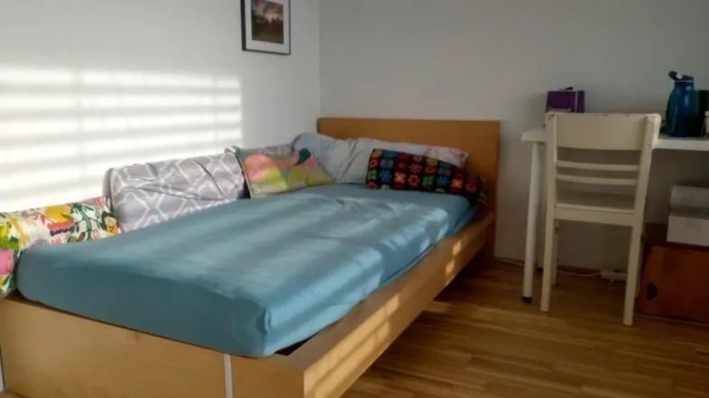 Helles Schlafzimmer mit Holzbett, Parkettboden und einem kleinen Bild an der Wand.