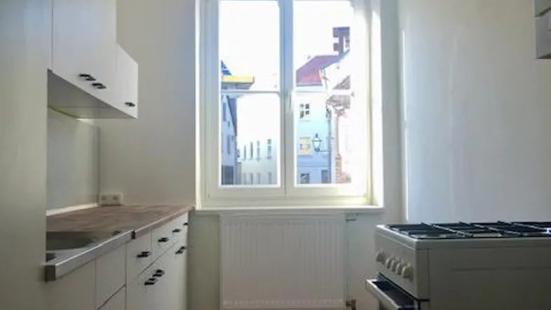 Schmale Küche mit weißen Schränken, Holz-Arbeitsplatte, Gasherd und einem Fenster.