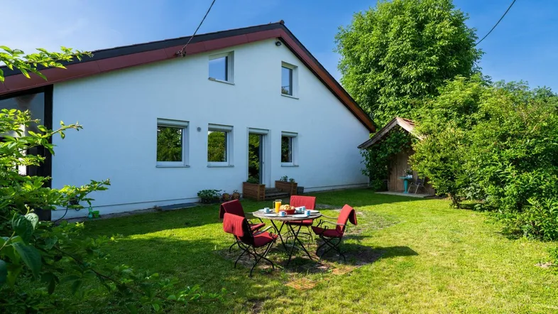 Heller Gartenbereich hinter dem Haus mit Rasenfläche und gemütlicher Sitzgruppe unter blauem Himmel.